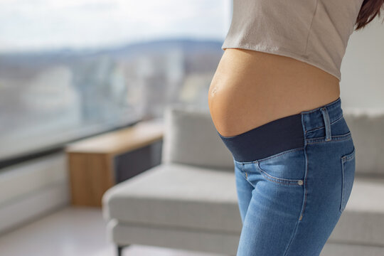 Maternity clothes pregnant woman wearing extensible full panel stretch jeans during pregnancy at home. Closeup of bump and clothing