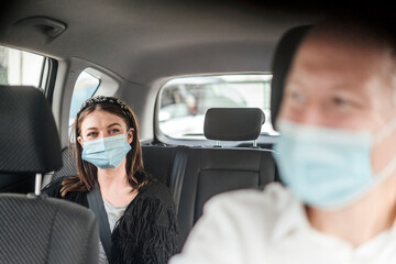 A woman wearing a protective mask on the back seat of a taxi car