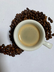Closeup of espresso with foam and coffee beans around on white background