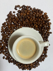 Closeup of espresso with foam and coffee beans around on white background