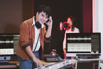 Asian producer standing by sound mixing console. Happy male music composer artist with a woman singer background