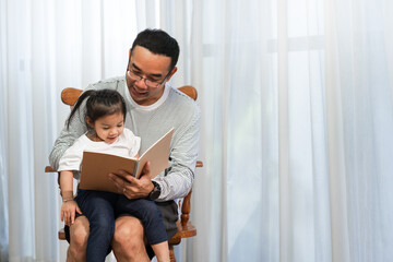 Asian father reading storybook to daughter in living room, family concept and early childhood development