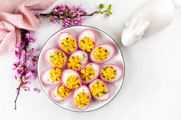 Stuffed Pink Boiled Deviled  Eggs with Paprika, pepper and mayonnketo. american, aise as an Appetizer, colored with beetroot. Easter food with easter bunny and spring flowers. Top view.