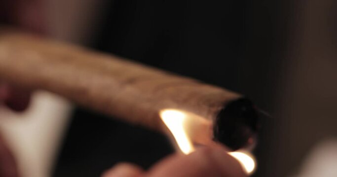 men's hands twist and set fire to a Cuban cigar with a match in their hands. macro