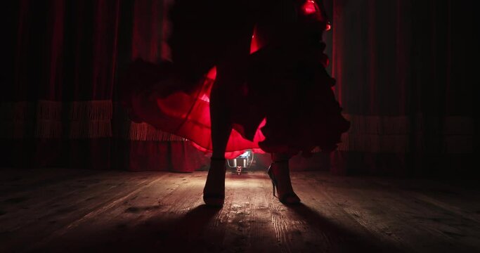 the legs of a woman twirling in a red dress with a large slit on high heels in the backlight. flamenco dance. the sound of heels. close-up