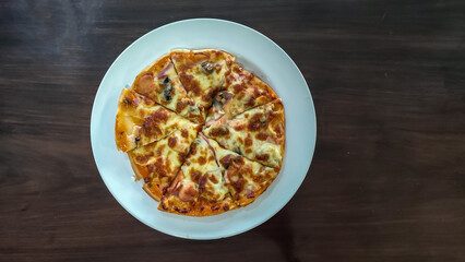 Crispy thin crust pizza with mushroom and sausage on white plate on wooden table