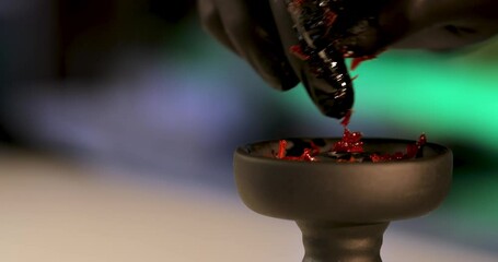 a hand in black mittens puts tobacco into the hookah bowl. the hookah man fills the hookah with red slime tobacco from above. macro
