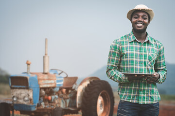 Success african male farmer in checkered shirt and straw hat holding digital tablet with smile and...