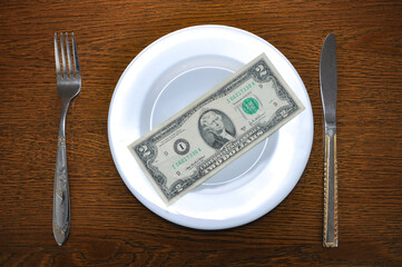 a denomination of 2 American dollars lies on a white plate. Photo describes the problem of rising prices in the global economy