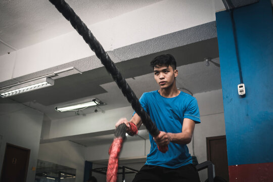 A fit young asian man doing an intense battle rope session. Cardiovascular training at the gym.
