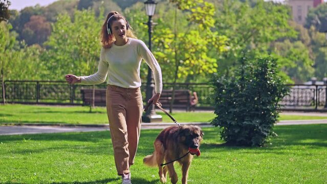 Positive beautiful woman listening to music and walking german shepherd dog