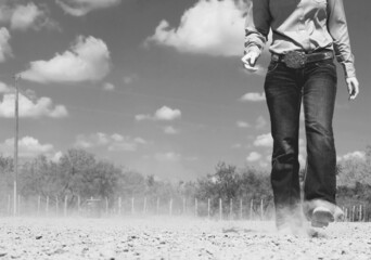 Western lifestyle with cowgirl walking through outdoor dirt arena in black and white.