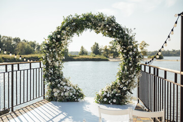 Obraz na płótnie Canvas Circle wedding arch decorated with white flowers and greenery outdoors.
