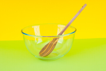 Empty glass food bowl with wooden spoon on green and yellow background