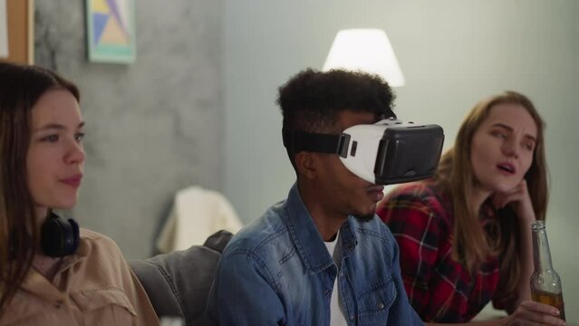 Bearded black guy with vr headset sits between pretty women during baseball match on tv closeup slow motion. Contemporary technology and sports show