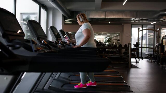 Overweight woman with headphones exercising on treadmill in gym