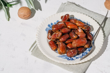 Dried dates and walnuts in a vintage plate on a white background . A sunny day.