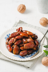 Dried dates and walnuts in a vintage plate on a white background . A sunny day.