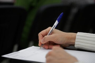 A woman with a blue fountain pen fills out a printed form, contract or resume. No face. Selective...