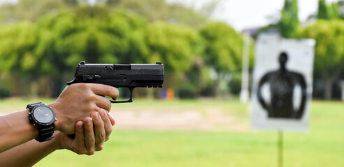 Automatic black 9mm pistol gun holding in hands of shooter and aiming to the man-target shooting paper ahead, concept for training and practising human to be body guard, vip protecting and gangsters.