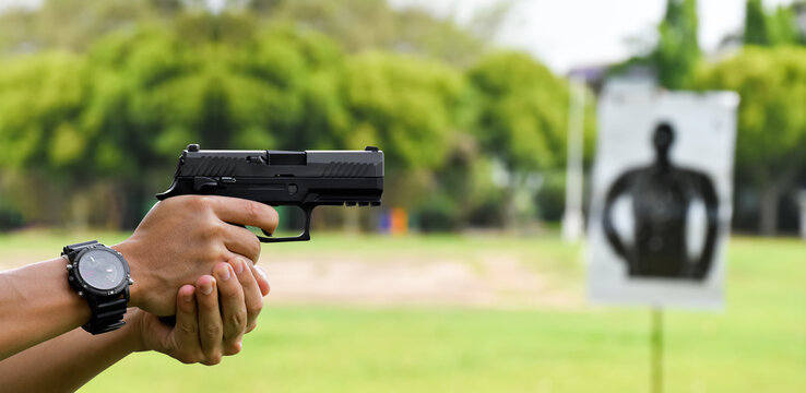 Automatic black 9mm pistol gun holding in hands of shooter and aiming to the man-target shooting paper ahead, concept for training and practising human to be body guard, vip protecting and gangsters.
