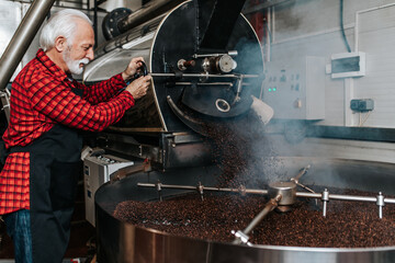 Senior man operating coffee roasting machine in coffee shop. Coffee industry.