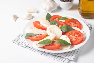 Delicious Italian caprese salad with sliced mozzarella, tomatoes, basil, pesto and garlic on background.