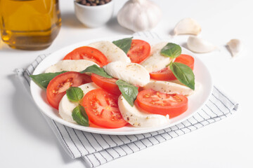 Delicious Italian caprese salad with sliced mozzarella, tomatoes, basil, pesto and garlic on background.