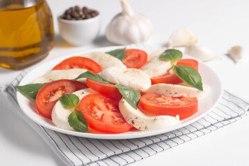 Delicious Italian caprese salad with sliced mozzarella, tomatoes, basil, pesto and garlic on background.