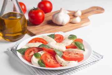 Delicious Italian caprese salad with sliced mozzarella, tomatoes, basil, pesto and garlic on background.