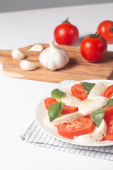 Delicious Italian caprese salad with sliced mozzarella, tomatoes, basil, pesto and garlic on background.