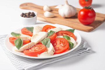 Delicious Italian caprese salad with sliced mozzarella, tomatoes, basil, pesto and garlic on background.