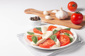 Delicious Italian caprese salad with sliced mozzarella, tomatoes, basil, pesto and garlic on background.