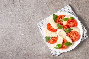 Delicious Italian caprese salad with sliced mozzarella, tomatoes, basil, pesto and garlic on background.