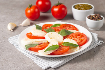 Delicious Italian caprese salad with sliced mozzarella, tomatoes, basil, pesto and garlic on background.
