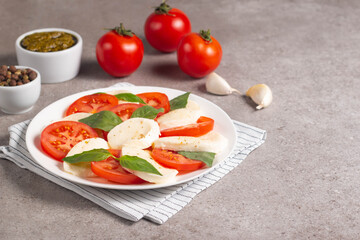 Delicious Italian caprese salad with sliced mozzarella, tomatoes, basil, pesto and garlic on background.