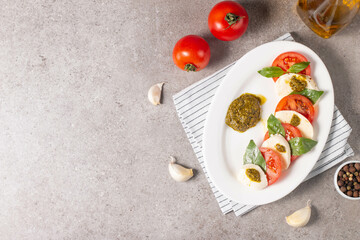 Delicious Italian caprese salad with sliced mozzarella, tomatoes, basil, pesto and garlic on background.
