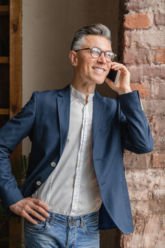 Vertical portrait of confident smiling caucasian mature middle-aged businessman in formal clothes talking on smart phone, calling his colleagues business partners in office work place