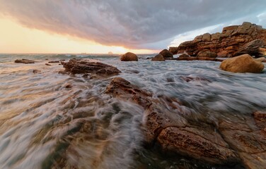 Beautiful sunrise scenery of a rocky beach on northern coast of Taiwan with golden sun rising on distant horizon & turbulent waves beating on rugged rocks under dramatic dawning sky (Long Exposure)