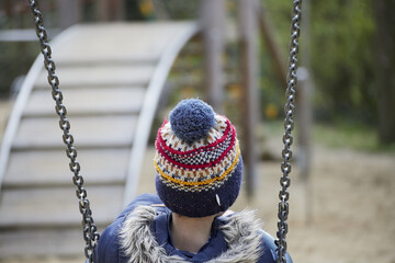 Closeup of a small boy in a winter outfit on the swing.
