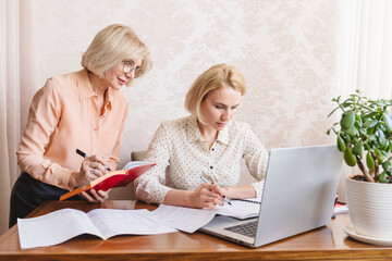 Mature business women discuss documents in the home office.