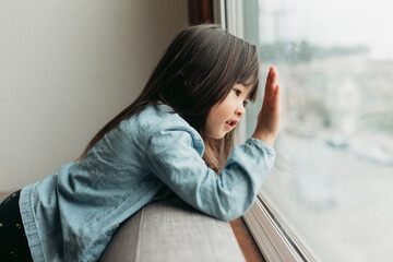 Multiracial girl looking out the window with a neighborhood view.