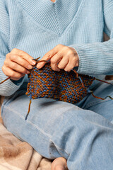 A 50-year-old woman lies on a woolen blanket and knits with wood