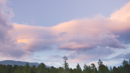 Hills with forest line on horizon under blue sky. Mountain range under cumulus clouds. Approach of rain front, deterioration of weather. Rays of sun break through dense layers of atmosphere. 