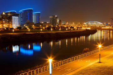 Fototapeta premium Riverside scenery of Taipei City at night with modern buildings & street lamp lights reflected on the water and the famous Huan Dong Rainbow Bridge over Keelung River at dusk in Taipei, Taiwan, Asia