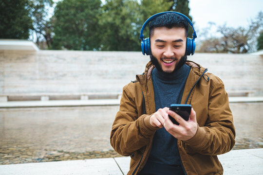 Smiling ethnic man using smartphone while listening to music