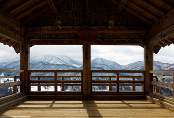 Fototapeta premium A scenic view overlooking the winter mountains covered with snow from inside Godaido Hall, one of the historical wooden architectures in Risshaku-ji Buddhist Temple in Yamadera, Yamagata, Japan
