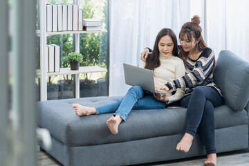 Lgbtqia. Two women use laptop computer on the sofa in the living room. Young Asian woman working with a laptop computer while sitting on the cozy sofa