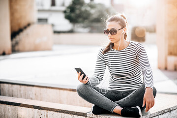 Young happy teen girl using a smart phone sititng in the city