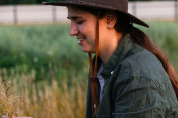 Defocus smiling young woman in cowboy hat. Girl in a cowboy hat in a field. Nature background. Closeup portrait caucasian girl smiling. Summertime. Fashion clothes. Side view. Out of focus